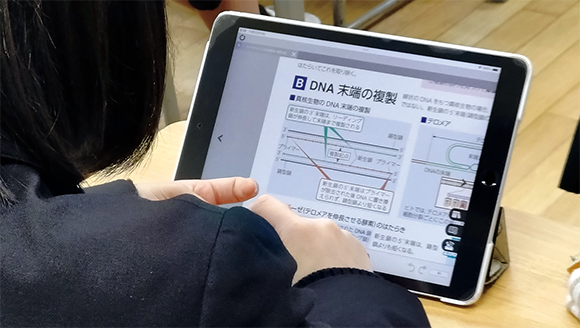 生物図録の紙面を開いて解説を聞く生徒